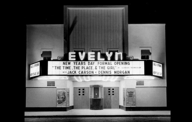 Black-and-white night photo of the Evelyn's brightly lit marquee. It reads: New Year's Day formal opening, The Time, the Place and the Girl, with Jack Carson and Dennis Morgan.