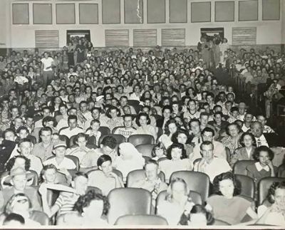 Black-and-white photo of a packed auditorium, row after row of men, women and children turned toward the camera.